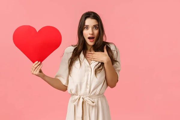 What an unexpected surprise. Love, relationship and valentines day concept. Touched and amazed tender lovely girlfriend receive heart card, looking amazed and astonished, pink background