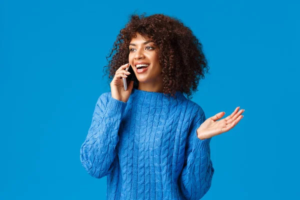 Carefree talkative attractive african-american woman in winter sweater discuss recent holidays and her trip abroad ski-resort, talking on phone, holding smartphone near ear gesturing, smiling