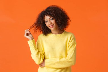Belden yukarı portre küstah ve seksi Afro-Amerikan kadın parmaklarını kıvırıp kıvırıyor başını eğiyor ve küstah cilveli gülüşlü, turuncu arka planda duran birine bakıyor.