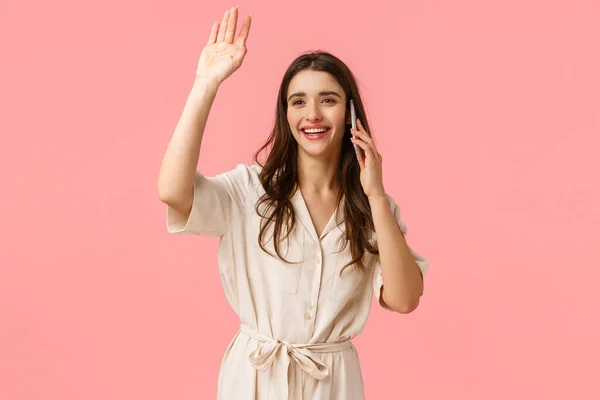 Alegre atraente sorrindo caucasiano mulher vendo amigo e acenando Olá, diga oi como falar ao telefone, falando, chamando alguém ter conversa e saudação transeunte, fundo rosa — Fotografia de Stock