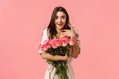 Şaşırmış kız şaşırmış ve sevgilisinin getirdiği güzel güllerden etkilenmiş. Çekici bir genç kadın, gülümseyen ve nefes nefese, nefes kesici bir buket, pembe arka plan