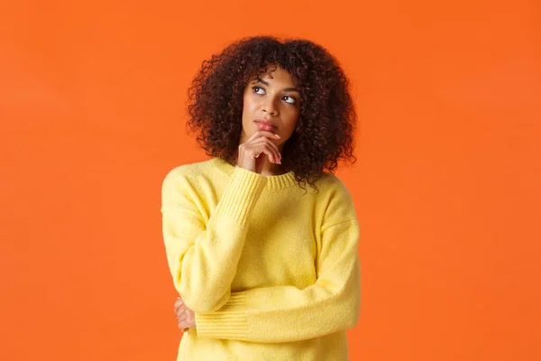 Waist-up portrait unsure, thoughtful young creative african-american female entrepreneur making new ideas, standing orange background, searching inspiration, thinking looking up