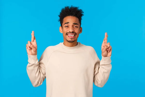 Nervös blyg och söt afrikansk-amerikansk kille med afro frisyr rädd berätta för föräldrar något stort, peka finger upp, krypa och ler med ängsliga uttryck, känsla av oro, blå bakgrund — Stockfoto