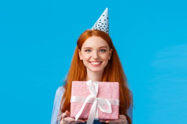 Waist-up portrait cheerful happy, pretty redhead, ginger girl celebrating birthday, receive cute pink wrapped present, wearing b-day cap and smiling, having fun at party, blue background clipart