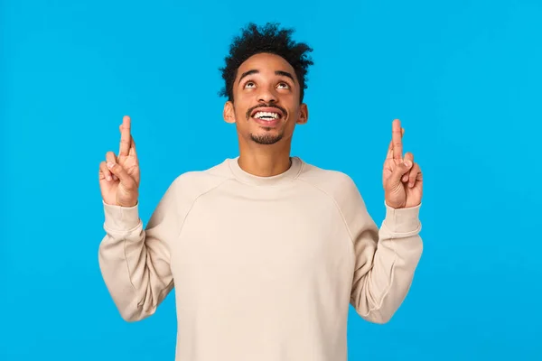 Enthusiastic and intrigued modern african-american male in white sweater, seeing something curious upwards, look and pointing fingers up, smiling astonished, wonder whats there, blue background — Stock Photo, Image