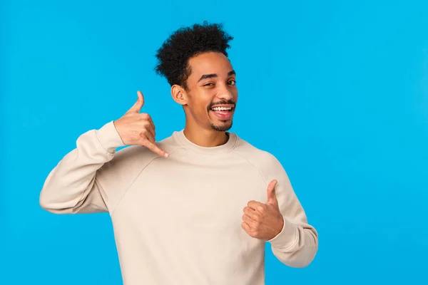 Call me later babe. Sassy and coquettish african-american confident macho guy with moustache, afro haircut showing thumb-up and phone gesture, wink and smiling flirty, blue background — Stock Photo, Image