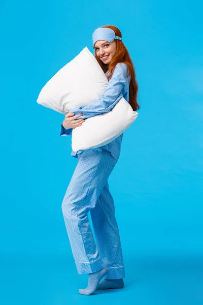 Tenderness, comfort and coziness concept. Full-length vertical shot tender and feminine lovely redhead girl in nightwear, sleep mask, hugging pillow giggling flirty and gazing camera with smile — Stock Photo, Image