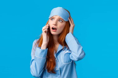 Telaşlı ve hayal kırıklığına uğramış, üzgün kızıl saçlı kız kötü haberlerle uyandı, telefonla arkadaşını aradı, akıllı telefonu kulağına tuttu, konuşuyordu huzursuz ve endişeli görünüyordu, mavi arka planı vardı.