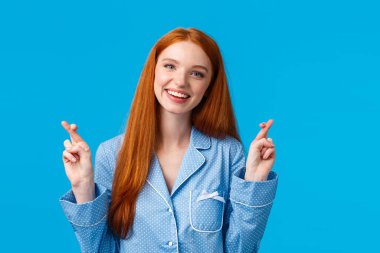 Umutlu, iyimser, gece giysisi içinde güzel bir kızıl kız, şans dileyin, başınızı eğin ve gülümseyin dilek dilerken, mucizeyi beklerken, hayaller gerçek olurken, mavi arka planda dururken.