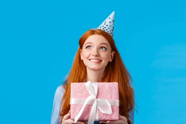 Весела мрійлива дівчина, що знімає всередині коробки на день народження. Симпатичний рудий гламурний підліток у чашці b-day, отримує прекрасний подарунок, тримає подарунок і виглядає у верхньому лівому куті щасливим і продуманим — стокове фото