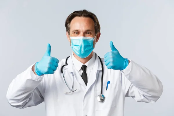Covid-19: 바이러스 예방, 의료 종사자 및 예방 개념. 의료용 마스크와 장갑을 착용하고 있는 중년의 의사가 만족 한 모습을 클로즈업 한 후 승인된 엄지 수술을 보여 주고 제품을 추천 한다. — 스톡 사진