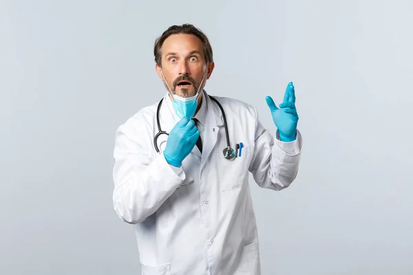 Covid-19: 바이러스 예방, 의료 종사자 및 예방 개념. 장갑을 끼고 충격을 받고 놀란 의사, 의료용 마스크벗기, 입을 다물고 있는 턱떨어지기, 하얀 배경 — 스톡 사진