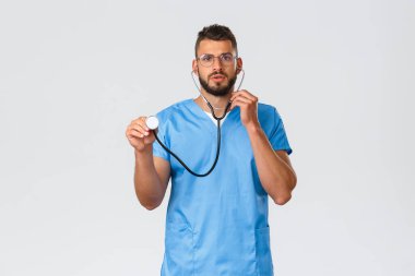Sağlık çalışanları, ilaç, covid-19 ve salgın kendini karantina konsepti. Endişeli genç doktor, önlüklü ve gözlüklü erkek hemşire, steteskopla tarama sırasında hasta dinliyor.
