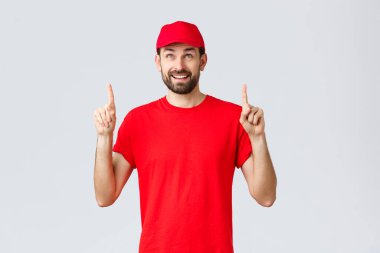 İnternetten alışveriş, karantina sırasında teslimat ve paket servis konsepti. Kırmızı tişörtlü neşeli kurye, şapkası parmakları havada. Çalışan, özel indirimle pankarta meraklı bakıyor