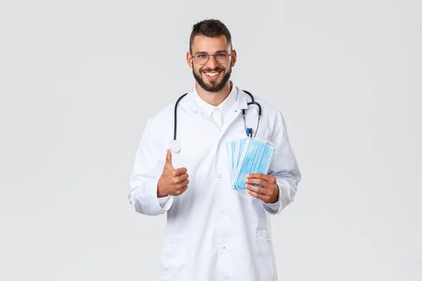 Εργάτες υγείας, ιατρική ασφάλιση, πανδημία και covid-19 έννοια. Όμορφος Ισπανός γιατρός με λευκό παλτό, στηθοσκόπιο, που δείχνει τον αντίχειρα προς τα πάνω και συνιστά να φοράτε ιατρική μάσκα — Φωτογραφία Αρχείου