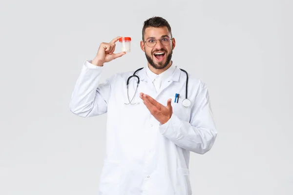 Healthcare workers, medical insurance, pandemic and covid-19 concept. Excited cheerful doctor in scrubs and glasses, showing medication, promote pills or medicine, smiling upbeat