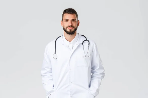 Travailleurs de santé, assurance médicale, laboratoire clinique et concept covid-19. Beau médecin en manteau blanc et stéthoscope, tenir la main dans les poches, sourire au patient, porter à l'hôpital — Photo