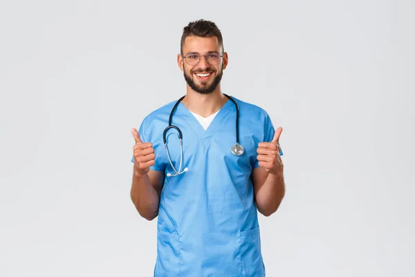 Healthcare workers, medicine, covid-19 and pandemic self-quarantine concept. Young friendly and supportive hispanic doctor, male physician or nurse in scrubs show thumb-up, recommend or approve — Stock Photo, Image