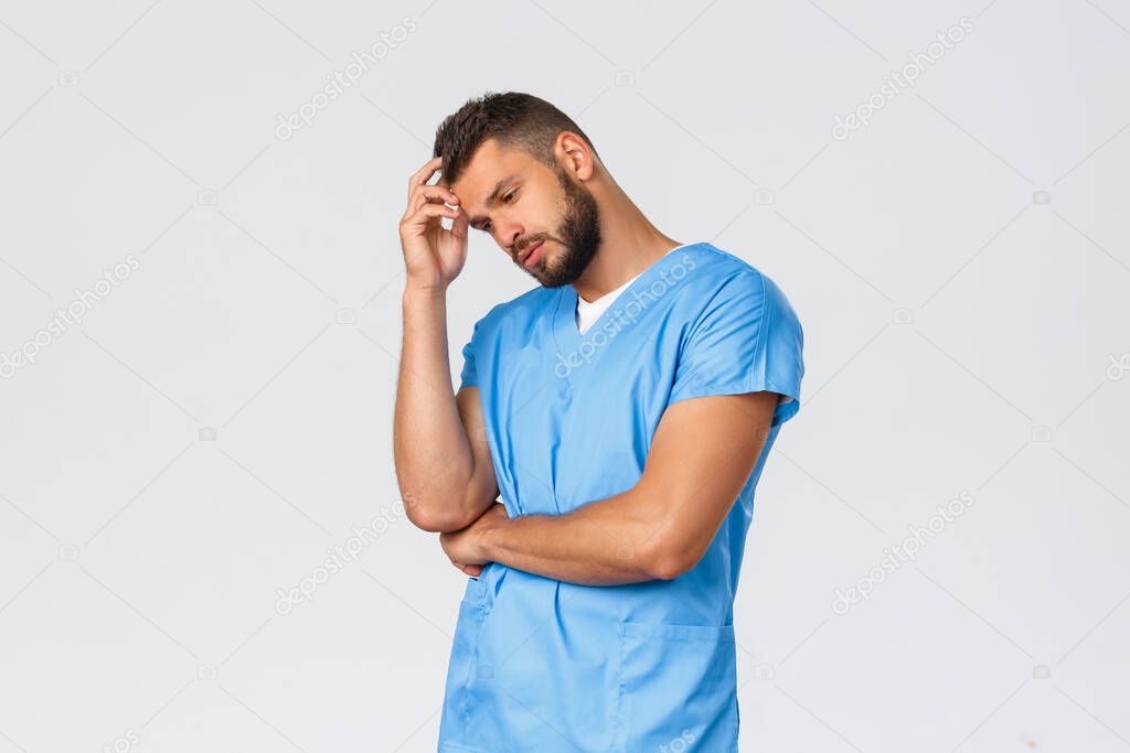 Healthcare workers, medicine, covid-19 and pandemic self-quarantine concept. Handsome thoughtful medical employee, doctor or physician in blue scrubs, look away, thinking or pondering decision