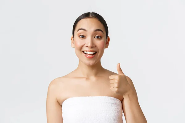 Beauty, cosmetology and spa salon concept. Satisfied happy asian female client in white towel showing thumbs-up and smiling pleased, recommend beauty salon, guarantee quality — Stock Photo, Image