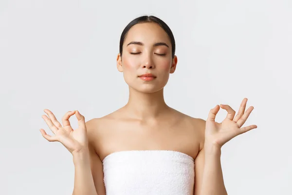 Skönhet, kosmetologi och spa salong koncept. Närbild av meditera avslappnad vacker asiatisk kvinna i vit handduk gör zen gest med slutna ögon, känna sig nöjd efter massage terapi — Stockfoto
