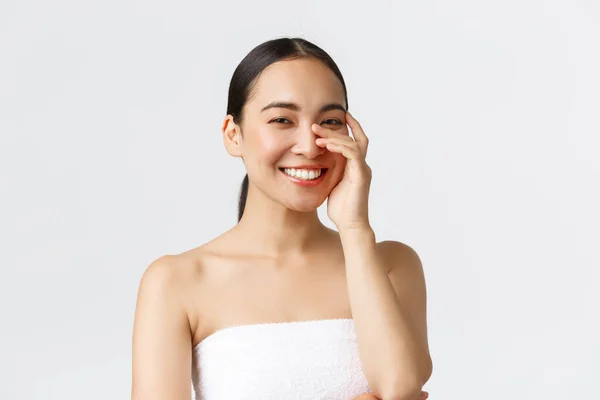 Kecantikan, kosmetologi dan konsep salon spa. Close-up dari wanita asia cantik di handuk mandi tertawa dan tersenyum gigi putih, lembut menyentuh wajah, kulit bersih dan skincare konsep — Stok Foto