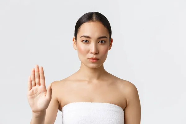 美容美发和温泉沙龙的概念。严肃而华丽的亚洲女人穿着浴巾，手牵着手停止姿势，拒绝或禁止某事，禁止治疗皮肤病产品，白色背景 — 图库照片