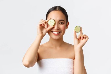 Güzellik, kişisel bakım, kaplıca salonu ve cilt bakımı konsepti. Elinde salatalık ve gülümseme, yüz veya vücut bakımının tanıtımı, kremin nemlendirici özellikleri.