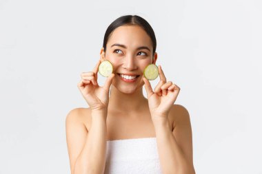 Güzellik, kişisel bakım, kaplıca salonu ve cilt bakımı konsepti. Elinde salatalık ve gülümseme, yüz veya vücut bakımının tanıtımı, kremin nemlendirici özellikleri.