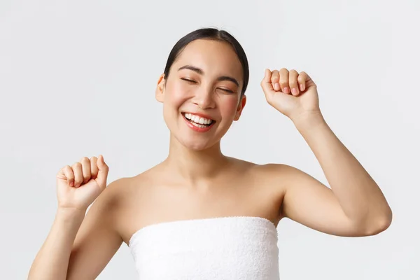 Beauty, cosmetology and spa salon concept. Close-up of beautiful carefree asian woman in bath towel, close eyes smiling happy and dancing as going shower, visit beauty clinic — Stock Photo, Image