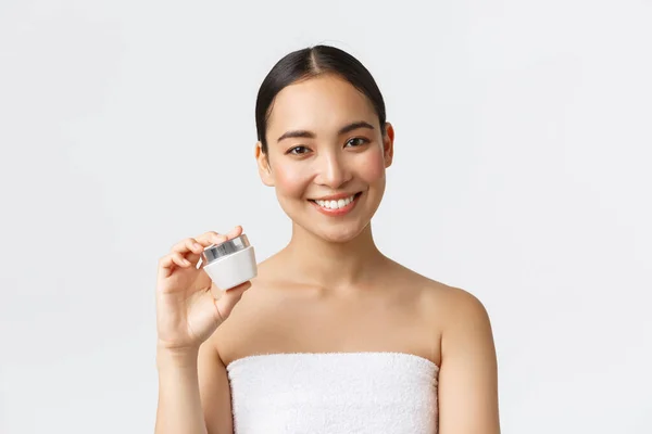 Szépség, testápolás, spa szalon és bőrápolás koncepció. Közelkép a gyönyörű ázsiai nő fürdőruha bemutató krém és mosolygós, ajánljuk hidratáló kezelés, fehér háttér — Stock Fotó