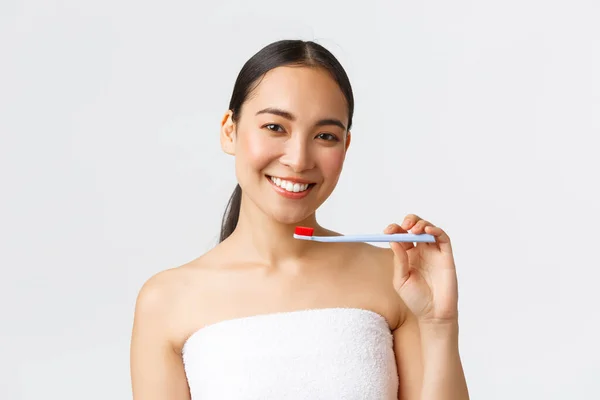 Kecantikan, perawatan pribadi, dan konsep kebersihan. Wanita Asia muda yang cantik dengan handuk mandi tersenyum gigi putih menunjukkan sikat gigi, menggunakan pasta gigi baru, merekomendasikan produk, latar belakang putih — Stok Foto