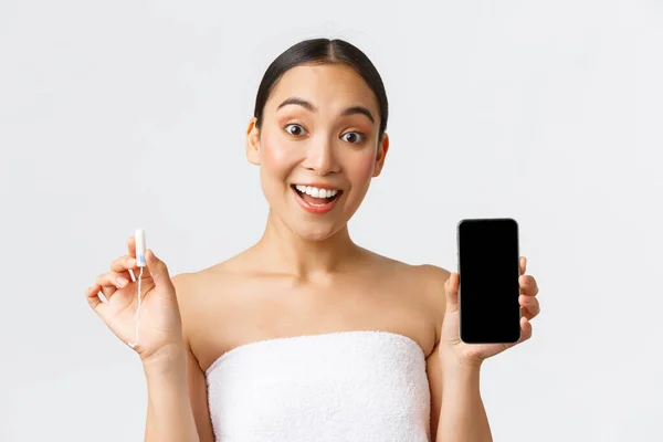 Beauty, personal and intimate care, mobile application concept. Cheerful smiling asian woman showing her menstrual cycle, period tracker on smartphone screen, holding tampon — Stock Photo, Image