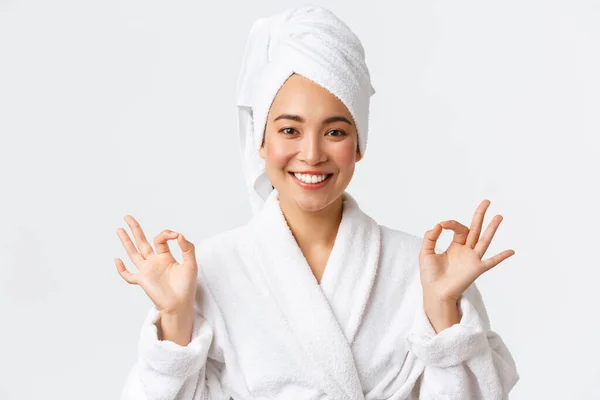 Cura personale, bellezza delle donne, bagno e doccia concetto. Primo piano di sollevato attraente donna asiatica partecipare spa salone di bellezza, indossare asciugamano da bagno e accappatoio, meditando, sensazione di nirvana, sorridente — Foto Stock