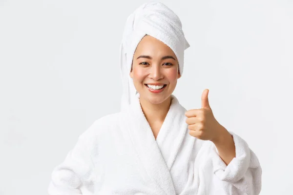 Personlig vård, kvinnlig skönhet, bad och dusch koncept. Nöjd glad asiatisk flicka i badrock och handduk visar tummen upp i godkännande, rekommenderar spa salong eller hygien produkt, ler glad — Stockfoto