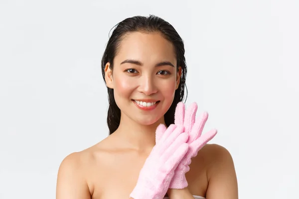 Cuidado personal, belleza de las mujeres, baño y ducha concepto. Atractiva chica asiática de pie ducha desnuda, con guantes de baño y sonriendo, lavado con exfoliantes corporales, de pie fondo blanco —  Fotos de Stock