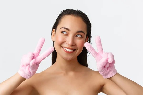 Personal care, women beauty, bath and shower concept. Close-up of dreamy beautiful asian girl standing naked and looking away thoughtful, showing peace signs while wearing bath gloves — Stock Photo, Image