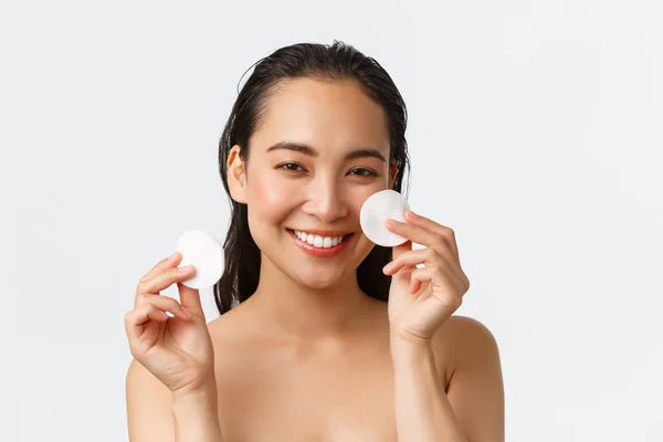 Skincare, kecantikan wanita, kebersihan dan konsep perawatan pribadi. Close-up of beautiful asian girl standing naked and show cotton pads near face, wipe-off makeup before shower, white background — Stok Foto