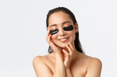 Cilt bakımı, kadın güzelliği, hijyen ve kişisel bakım konsepti. Yumuşak, çıplak Asyalı kadın spa günü, kapalı gözler ve dokunmuş ten gibi gülümseme, göz bantları altında uygula, kolajen maskesi