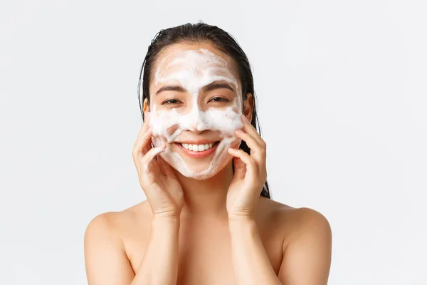 Skincare, kecantikan wanita, kebersihan dan konsep perawatan pribadi. Close-up of beautiful asian female standing naked in shower, apply skin cleansing foam and smile, feeling fresh and upbeat — Stok Foto