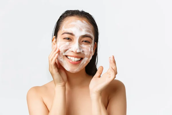 Bőrápolás, női szépség, higiénia és testápolás. Közelkép boldog mosolygós ázsiai nő áll meztelenül a kádban, a napi ellátás bőr tisztító hab és keres örömteli, fehér háttér — Stock Fotó