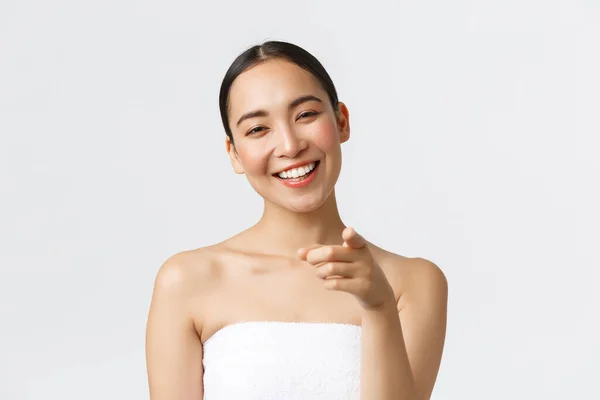 Beauty, cosmetology and spa salon concept. Close-up or attractive asian woman in towel smiling happy and pointing finger at camera, recommend you visit beauty clinic, white background — Stock Photo, Image