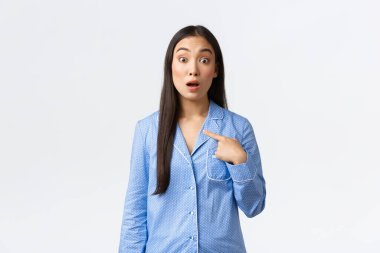 Mavi pijamalı sürpriz Asyalı kadın kendini işaret ediyor ve şaşkın şaşkın bakıyor, sorular soruyor, bahsi geçiyor veya seçiliyor, beyaz arka planda belirsiz duruyor. Kız kendi adını duyunca hayrete düşüyor.