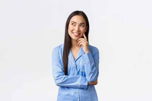 Sonhador pensativo menina asiática em pijama azul com ideia interessante, olhando canto superior esquerdo no comentário bolha, sorrindo satisfeito como pensar, sonhando acordado antes de ir para a cama, fundo branco — Fotografia de Stock