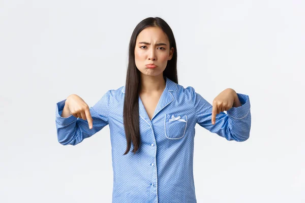 Decepcionado molesto y sombrío chica asiática quejándose, haciendo pucheros triste y mirando a la cámara disgustado como señalando con los dedos hacia abajo. A la mujer no le gusta la fiesta de pijamas, sentirse deprimida, fondo blanco — Foto de Stock