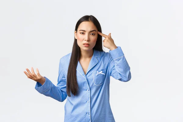 Arrogante ragazza asiatica guardando frustrato e perplesso, indossando pigiama blu, guardando con disprezzo come toccare il tample e sollevare la mano confuso, rimproverando qualcuno che si comporta stupido o pazzo — Foto Stock