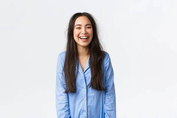 Sorrindo feliz e energizado menina asiática com cabelos bagunçados vestindo pijama e rindo, acordando entusiasta e alegre, tendo boa noite de sono, de pé fundo branco — Fotografia de Stock