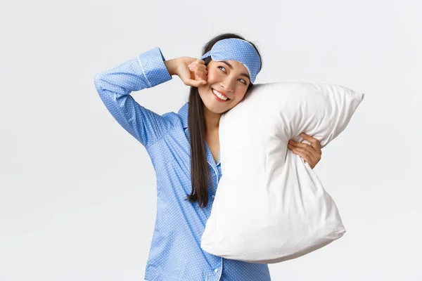 Leende glad asiatisk flicka i sovmask och pyjamas, liggande i sängen och krama kudde, stretching som vakna med intressant idé, tittar övre vänstra hörnet på promo banner glad — Stockfoto