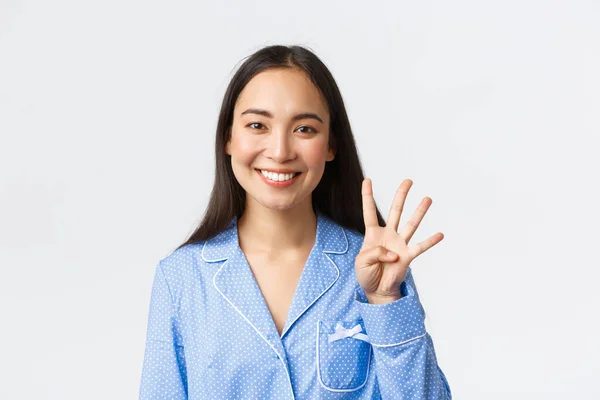 Close-up tiro de feliz atraente asiático mulher em azul pijama mostrando quatro dedos e sorrindo dentes brancos, explicar regras principais ou fazer a ordem, de pé fundo branco encantado — Fotografia de Stock