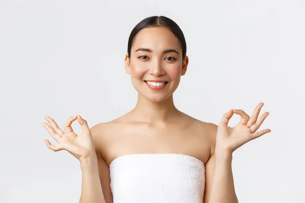 Beauty, cosmetology and spa salon concept. Close-up of beautiful female asian in beauty clinic standing towel and show zen, lotus gesture with smile, satisfied after massage, white background — Stock Photo, Image